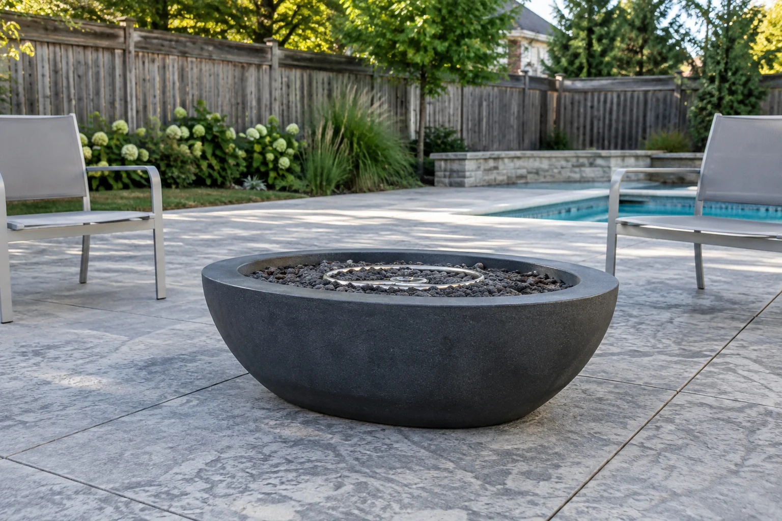 Gas fire bowl on a stone patio beside a backyard pool